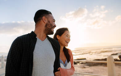 Fröhliches Paar, das am Meer spazieren geht und sich an den Händen hält; Mann und Frau genießen ihren Urlaub am Meer. - JLPSF28270