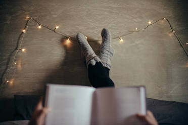 Ausschnitt einer Frau, die mit einem Buch auf dem Bett liegt, Fokus auf weibliche Beine an der Wand. - JLPSF28288