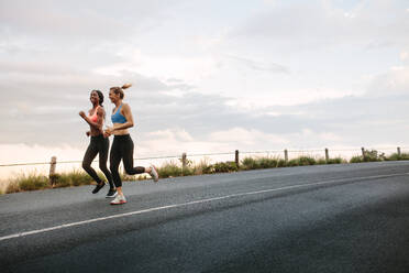Two women athletes running on road early in the morning with cloudy sky in the background. Fitness women jogging on road. - JLPSF28292