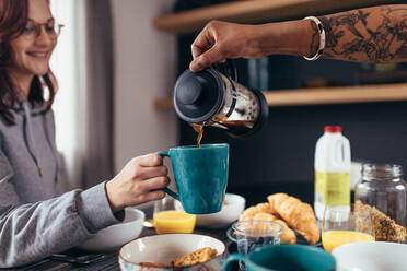 Nahaufnahme eines Freundes, der seiner Freundin Kaffee in die Tasse gießt. Ein Paar frühstückt zusammen am Morgen. - JLPSF28295