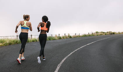 Rear view of two women athletes running on road early on a foggy morning. Fitness women jogging on road. - JLPSF28296