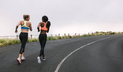 Rückansicht von zwei Sportlerinnen, die an einem frühen nebligen Morgen auf der Straße laufen. Fitness-Frauen joggen auf der Straße. - JLPSF28296