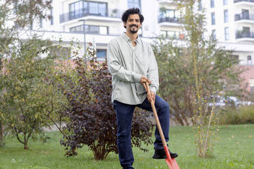 Smiling man with shovel standing by plant in garden - SGF02926