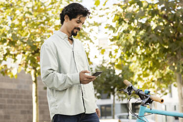 Lächelnder Mann mit Smartphone in der Nähe eines Fahrrads - SGF02928