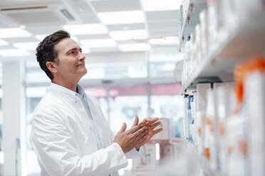 Pharmacist examining medicines on shelf in pharmacy - JOSEF14551