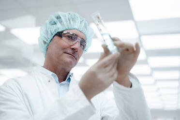 Chemist wearing protective eyewear analyzing test tube in laboratory - JOSEF14562