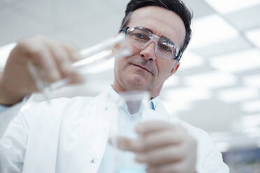 Chemiker gießt eine Chemikalie aus einem Reagenzglas in einen Kolben im Labor - JOSEF14565