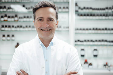 Happy pharmacist in front of medicines on shelf at store - JOSEF14567