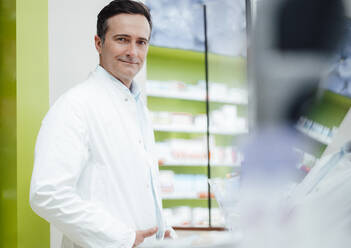 Smiling pharmacist wearing lab coat in pharmacy - JOSEF14575