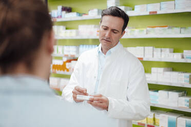 Apotheker, der vor einem Kunden in der Apotheke ein Medikament untersucht - JOSEF14585