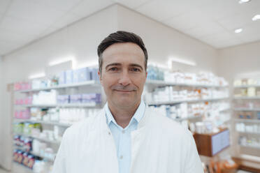 Smiling pharmacist in front of medicines shelf at pharmacy - JOSEF14589