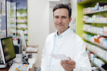 Smiling mature pharmacist showing prescription at store - JOSEF14606