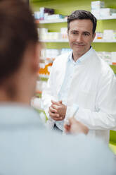 Lächelnder Apotheker, der einem Kunden ein Medikament im Laden zeigt - JOSEF14610