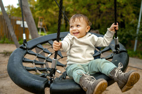 Glückliches süßes Baby Junge schwingt auf Nest Schaukel im Herbst Park - ANAF00451