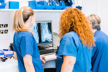 Mature nurse with colleagues examining x-ray image on computer at hospital - MMPF00447