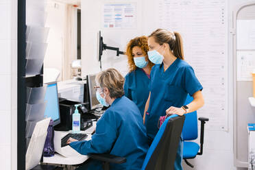 Mature nurse with colleagues discussing through computer at hospital - MMPF00455