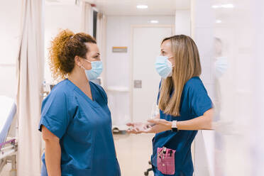 Nurses wearing masks talking with each other at hospital - MMPF00470