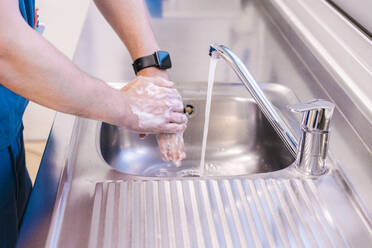 Doctor washing hands with water in sink at hospital - MMPF00485