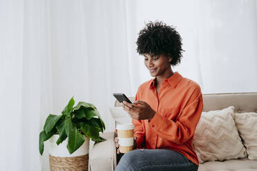 Smiling young freelancer using smart phone on sofa at home - EBBF06843