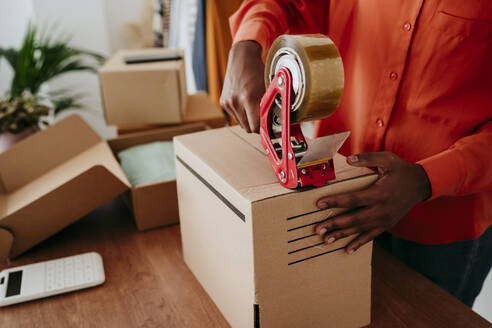 Hands of businesswoman sealing packages with tape at desk - EBBF06846