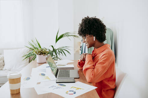 Smiling businesswoman using laptop with documents on desk at home office - EBBF06868