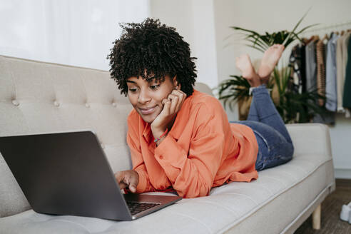 Freelancer lying on sofa and using laptop at home office - EBBF06907