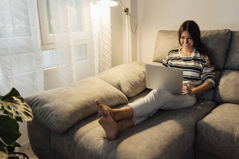 Glückliche Frau mit Laptop auf dem Sofa zu Hause - EGHF00615