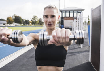 Lächelnde Sportlerin beim Training mit Hanteln an einem sonnigen Tag - UUF27725