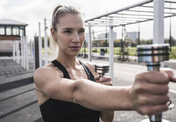 Junger Sportler beim Training mit Hanteln an einem sonnigen Tag - UUF27726