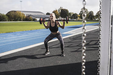 Young sportswoman exercising with barbell by running track - UUF27728