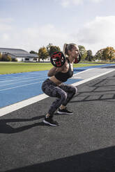 Athlete exercising with barbell by running track - UUF27729