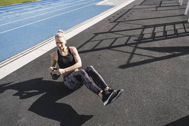 Young athlete exercising with kettlebell at sports track on sunny day - UUF27734