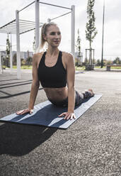 Smiling young sportswoman doing cobra pose on exercise mat - UUF27751