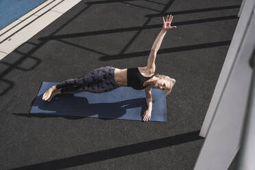 Young sportswoman practicing side plank yoga pose on exercise mat - UUF27758