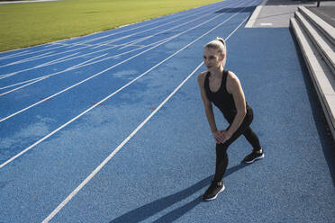 Young sportswoman doing warm up exercise on running track - UUF27791