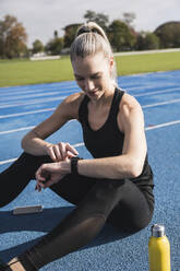 Lächelnde junge Sportlerin mit Smartwatch auf der Strecke - UUF27797