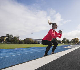 Sportswoman with wireless headphones doing jumping exercise on track - UUF27801