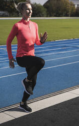 Young sportswoman doing warm up exercise at running track - UUF27802