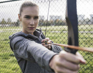 Selbstbewusste Sportlerin beim Bogenschießen am Zaun - UUF27808