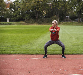 Young sportswoman practicing with kettle bell on running track - UUF27820