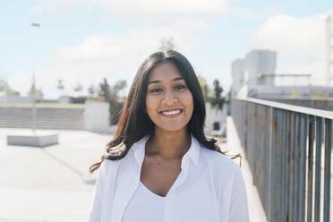 Happy young woman standing by railing on sunny day - MEUF08330