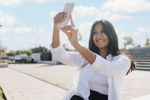 Glückliche junge Frau nimmt Selfie durch Smartphone - MEUF08333