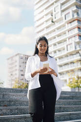 Smiling woman using mobile phone on steps - MEUF08335