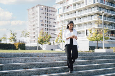 Young woman using smart phone and walking on steps - MEUF08337