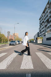 Junge Frau beim Überqueren der Straße an einem sonnigen Tag - MEUF08357