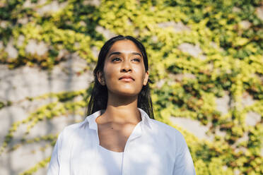 Contemplative young woman standing in front of plants - MEUF08361