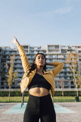 Woman with arms raised standing in front of building - MEUF08396