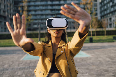 Junge Frau gestikuliert mit Virtual-Reality-Simulator an einem sonnigen Tag - MEUF08405