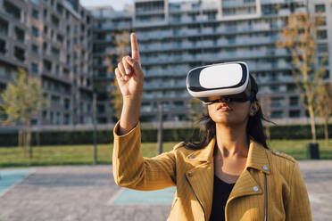 Junge Frau gestikuliert mit einem Virtual-Reality-Simulator vor einem Gebäude - MEUF08406