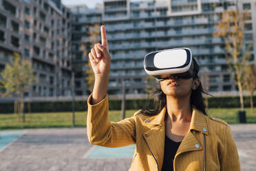 Young woman gesturing with virtual reality simulator in front of building - MEUF08406